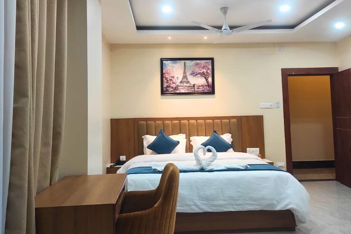 A hotel room with a bed, a desk, a chair, a ceiling fan, recessed lighting, and a painting on the wall.