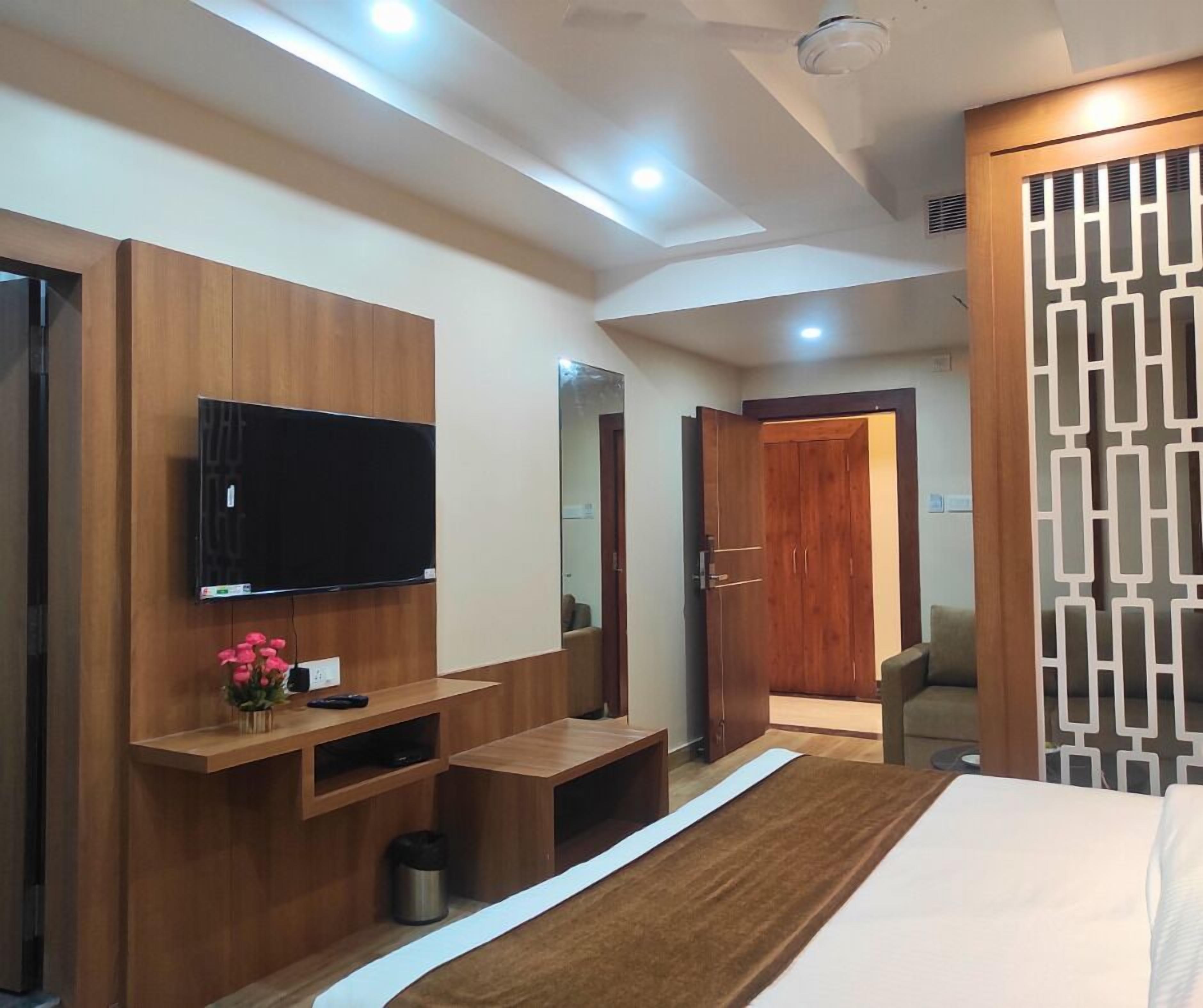 A modern hotel room with a large bed, a TV mounted on the wall, a wooden cabinet, and a decorative mirror.