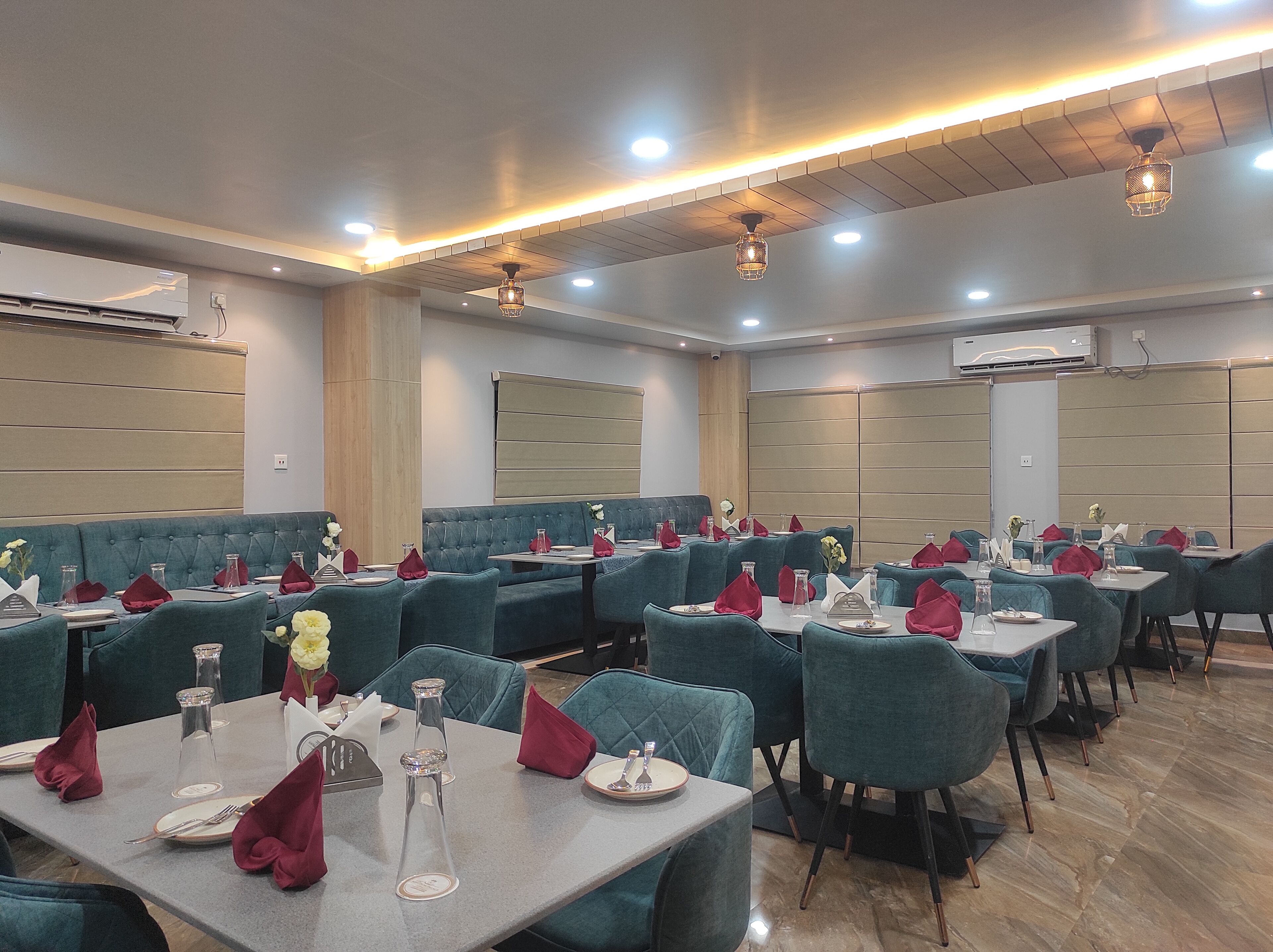 Un restaurante con cabinas tapizadas en color verde azulado y mesas dispuestas con servilletas rojas, cristalería transparente y platos blancos.