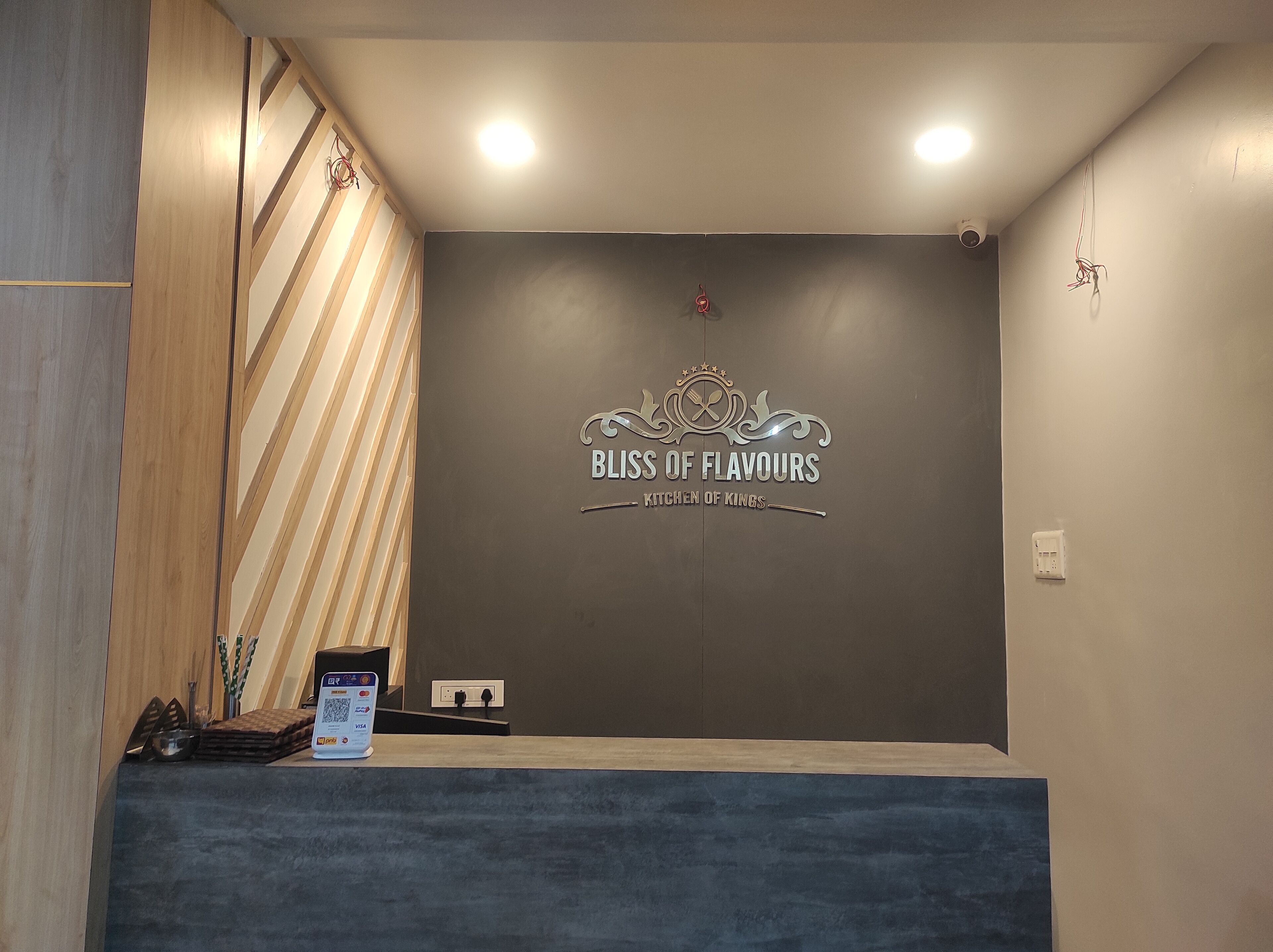 Un mostrador de recepción con un letrero que dice "BLISS OF FLAVORS KITCHEN OF KINGS" y un código QR para el registro.