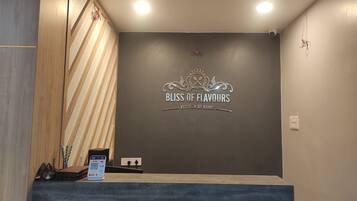 Un mostrador de recepción con un letrero que dice "BLISS OF FLAVORS KITCHEN OF KINGS" y un código QR para el registro.