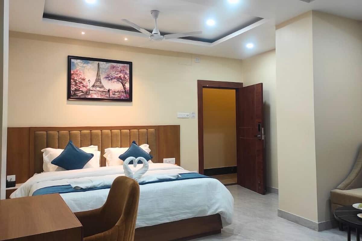 A modern hotel room with a large bed, a ceiling fan, recessed lighting, a painting of a cherry blossom tree, and a wooden door.