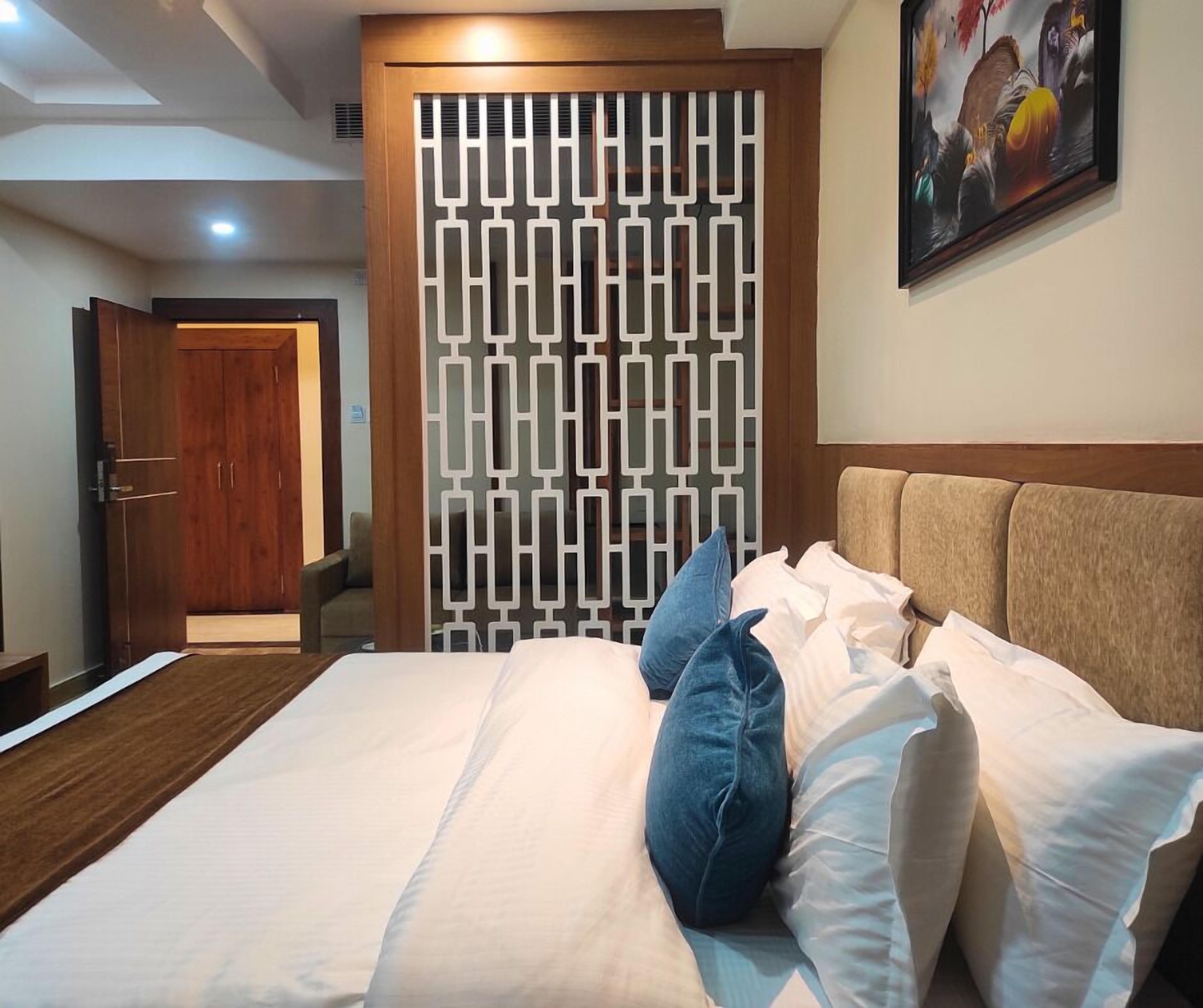 Habitación de hotel con una cama, una puerta de madera, un biombo decorativo y un cuadro en la pared.
