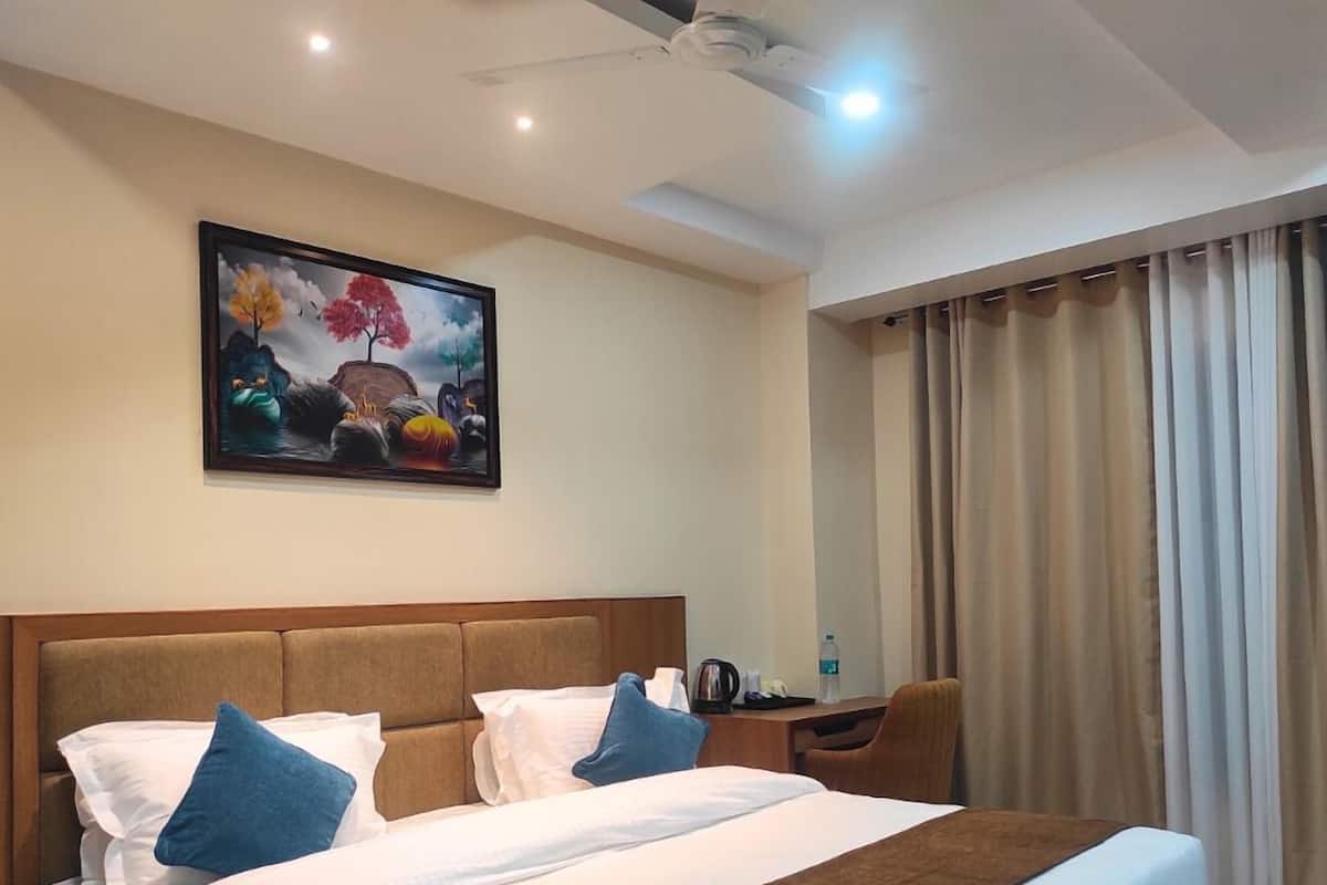 A hotel room with a large bed, two pillows, a nightstand, a desk, a chair, a painting on the wall, and a window with curtains.