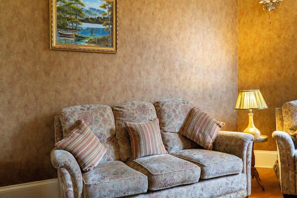 A cozy living room with a floral-patterned sofa, a lamp, and a painting on the wall. - Killean Farmhouse (Inveraray)