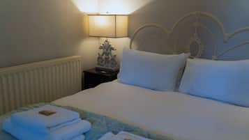 A neatly made bed with white linens and a decorative headboard, a bedside lamp, and a folded towel on the nightstand.