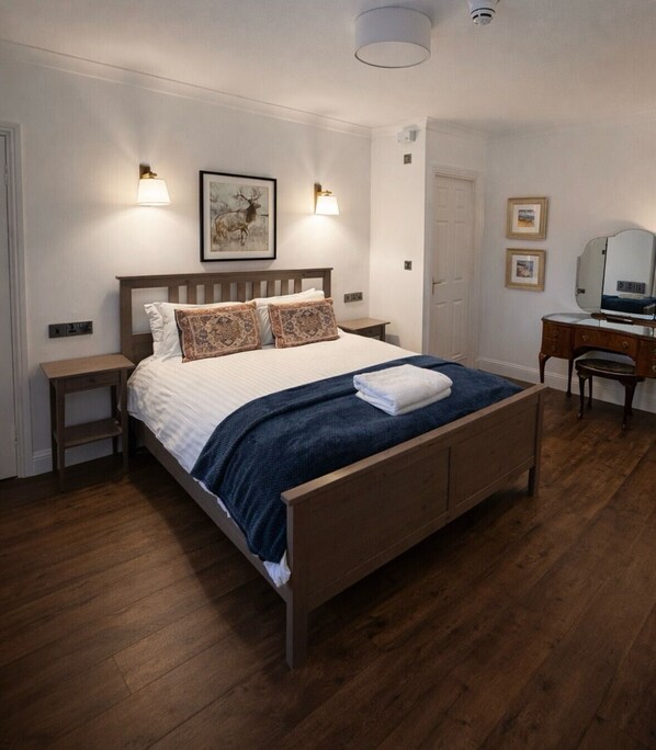 A neatly arranged bedroom with a wooden bed, two bedside tables, a dresser, and a mirror. - Killean Farmhouse (Inveraray)