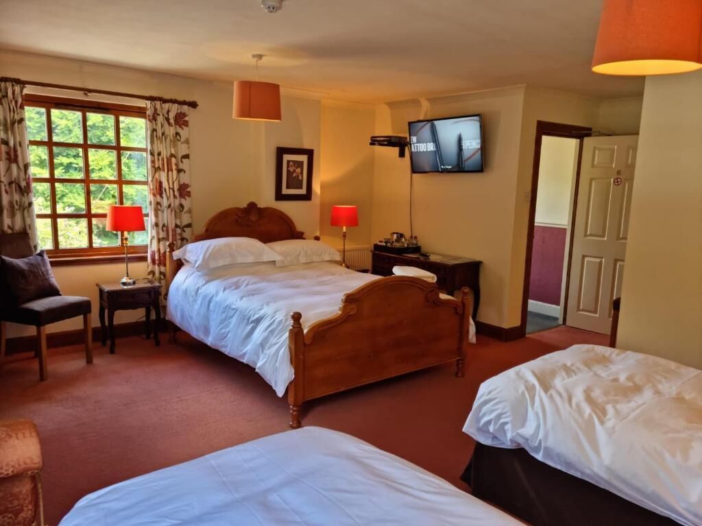 Une chambre d’hôtel avec deux lits simples, une tête de lit en bois, une télévision, une fenêtre avec des rideaux et une porte.