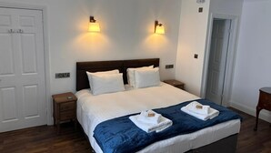 A hotel room with a large bed, two bedside lamps, a wooden nightstand, and a door. - Killean Farmhouse (Inveraray)