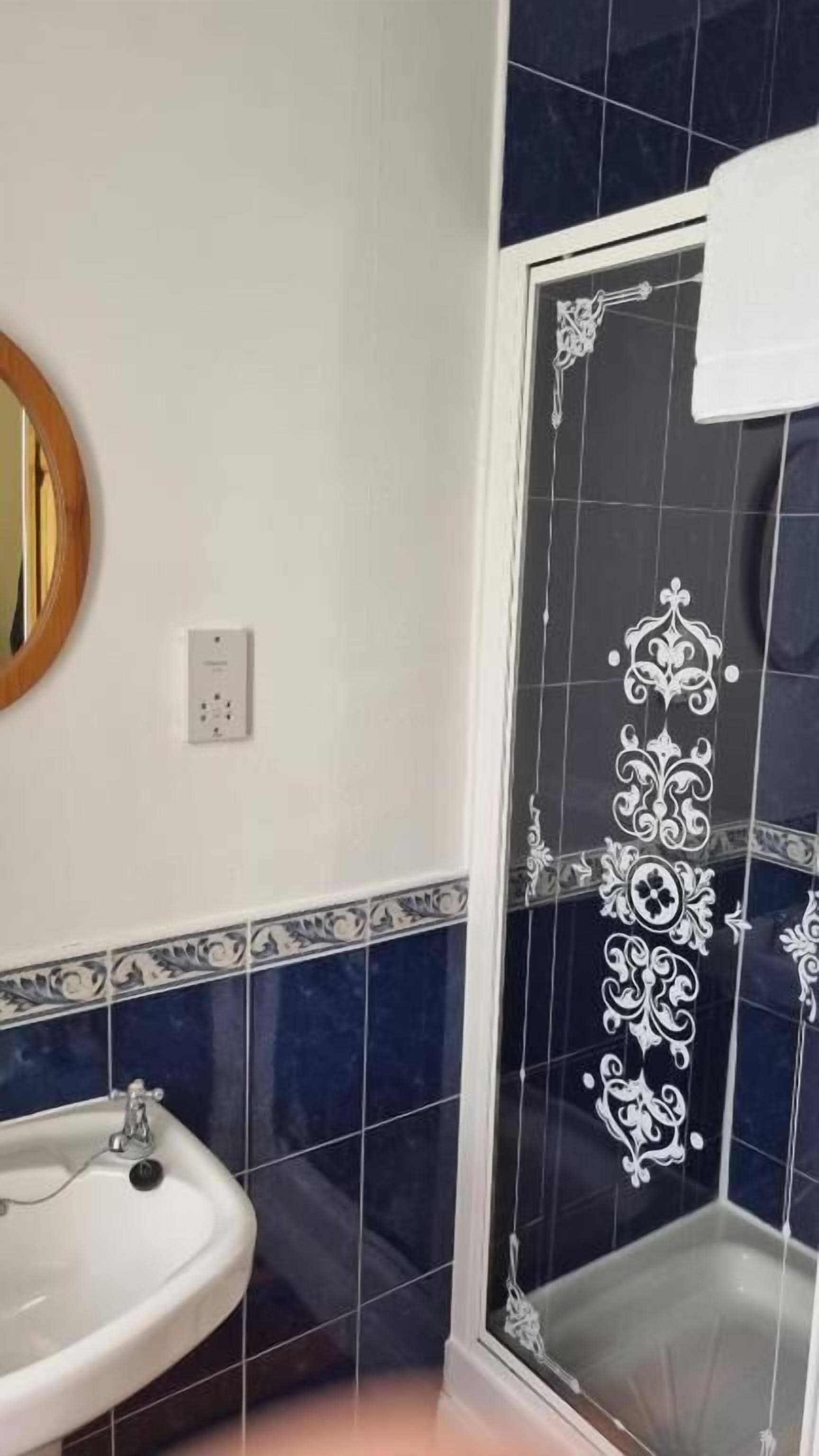A bathroom with a white sink, a mirror, and a shower with decorative tiles.