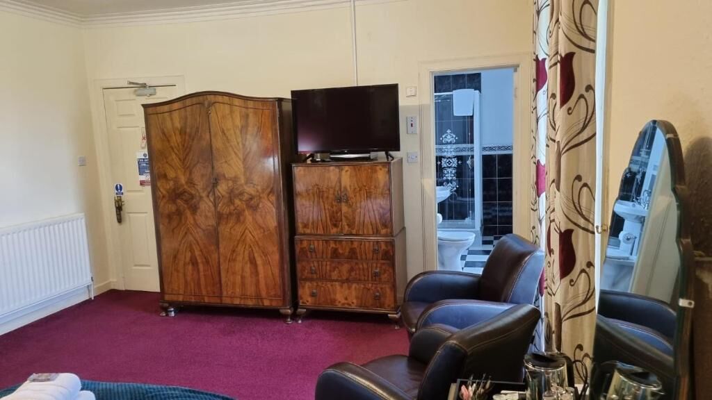 Una habitación con un amplio armario de madera, un televisor sobre una cómoda y una zona de estar con alfombra morada.