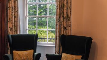 Two dark green armchairs with floral cushions, positioned in front of a window with a view of greenery.