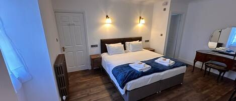 A hotel room with a large bed, bedside tables, a desk with a chair, and a mirror.