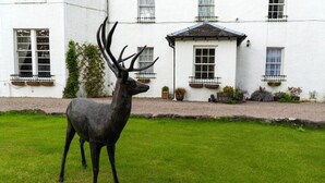 A deer statue in front of a white building with multiple windows and balconies. - Killean Farmhouse (Inveraray)