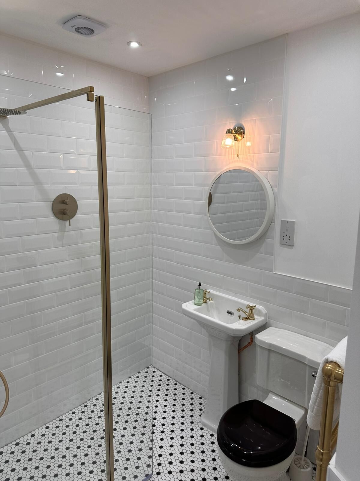 Un baño moderno con azulejos blancos tipo metro, cerramiento de ducha de vidrio, lavamanos pedestal y retrete.