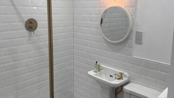 Un baño moderno con azulejos blancos tipo metro, cerramiento de ducha de vidrio, lavamanos pedestal y retrete.