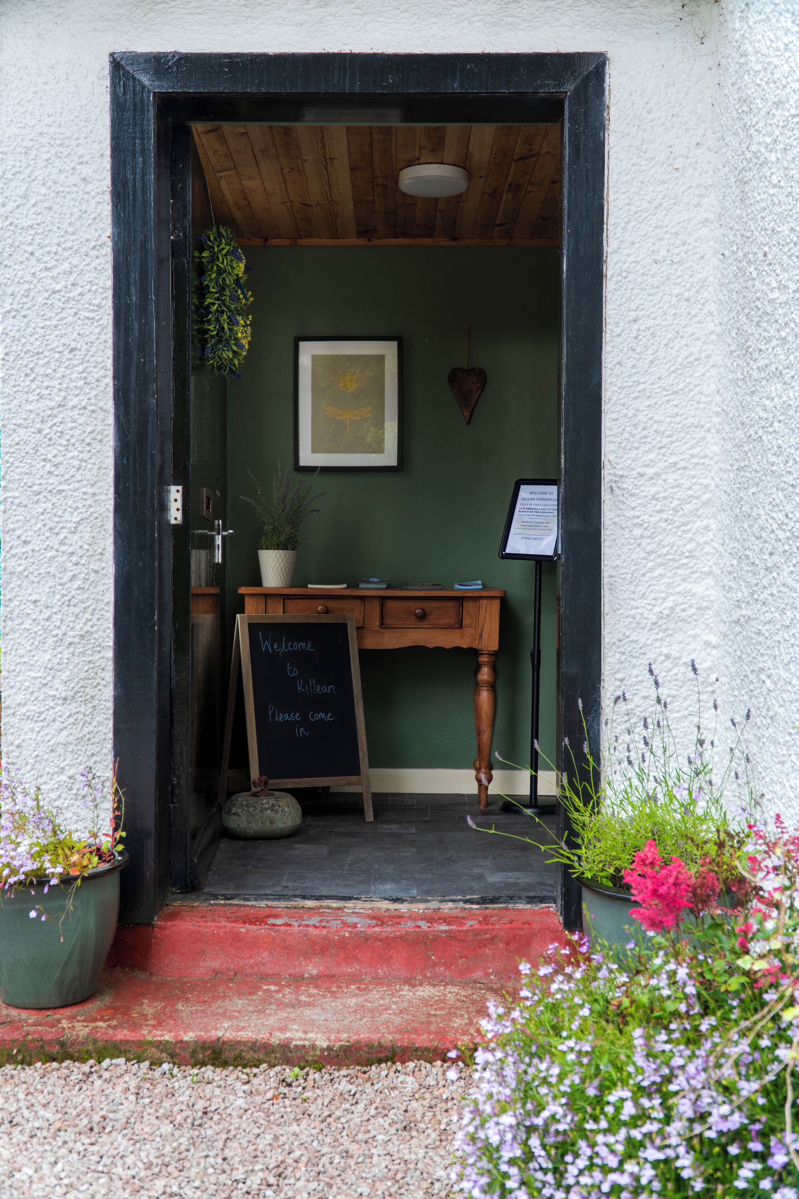 A doorway with a chalkboard sign, wooden furniture, and potted plants.