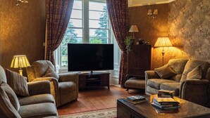 A living room with a large flat-screen TV, two sofas, a coffee table with books, and a wooden cabinet. - Killean Farmhouse (Inveraray)
