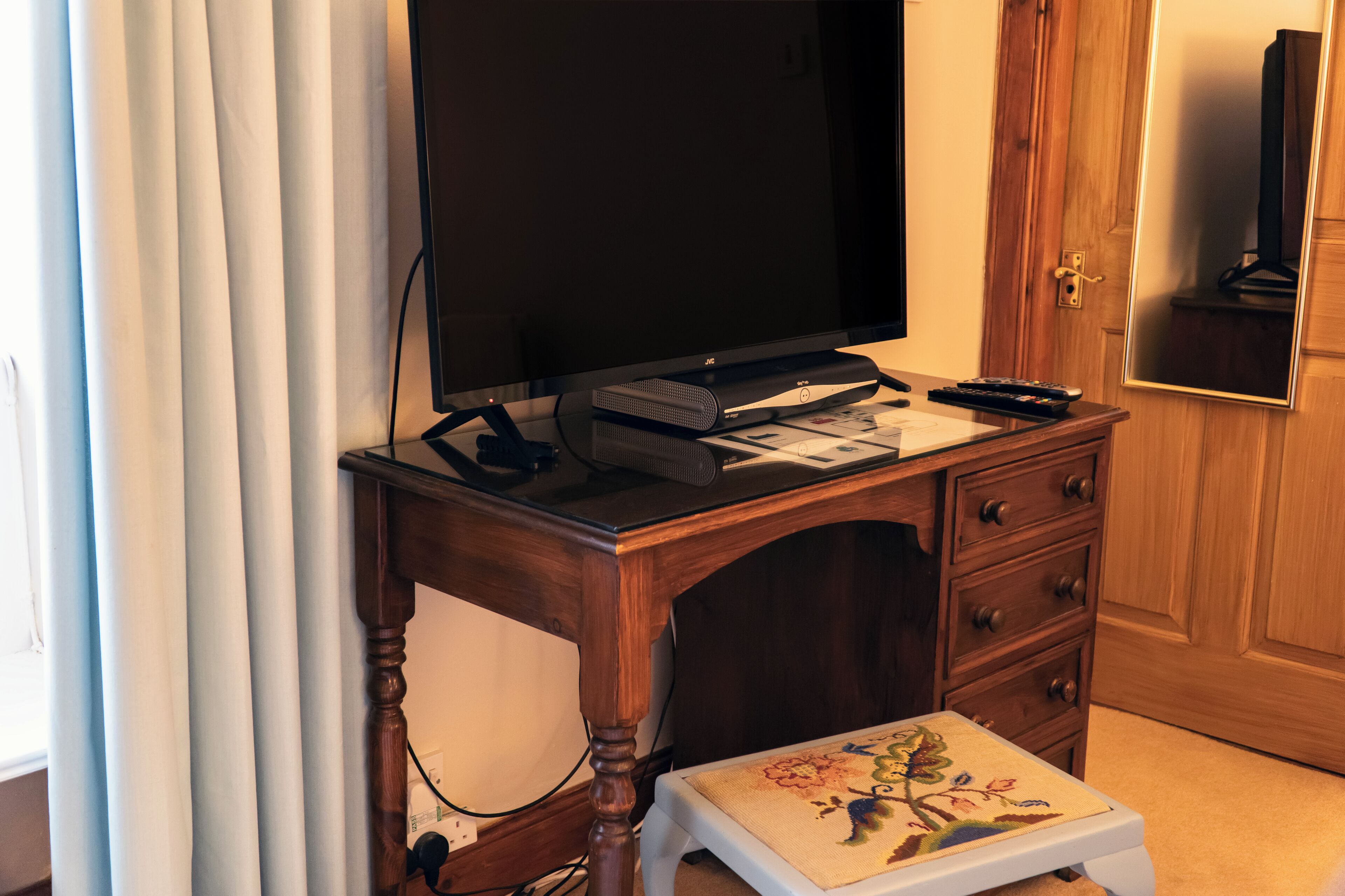 A wooden desk with a flat-screen TV, a speaker, and a remote control.