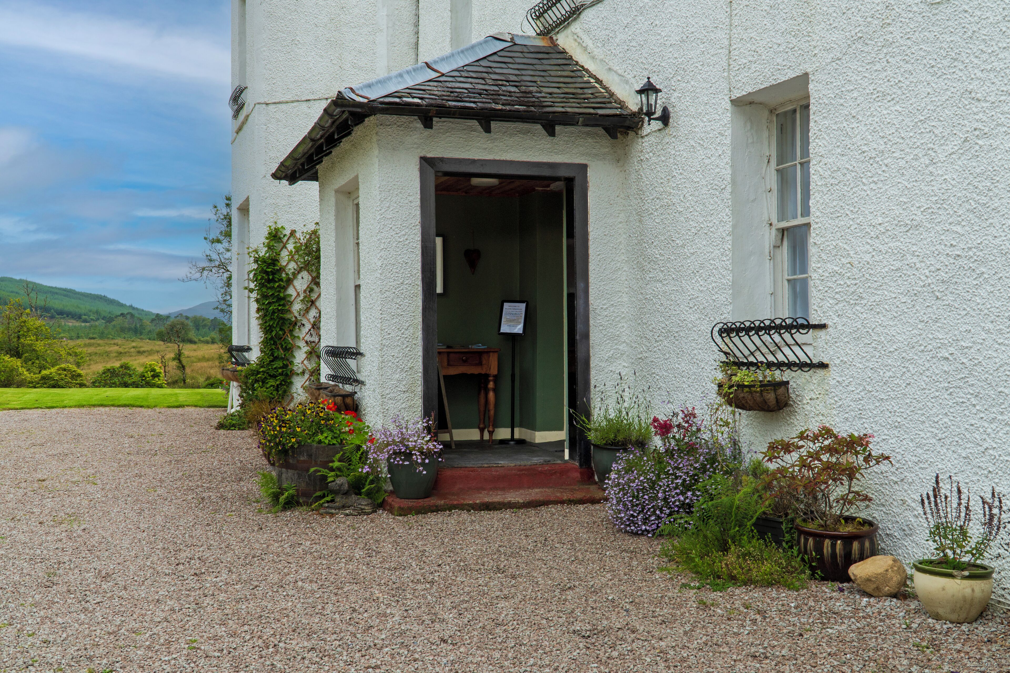 A white building with a gravel driveway, a wooden door, and potted plants.
