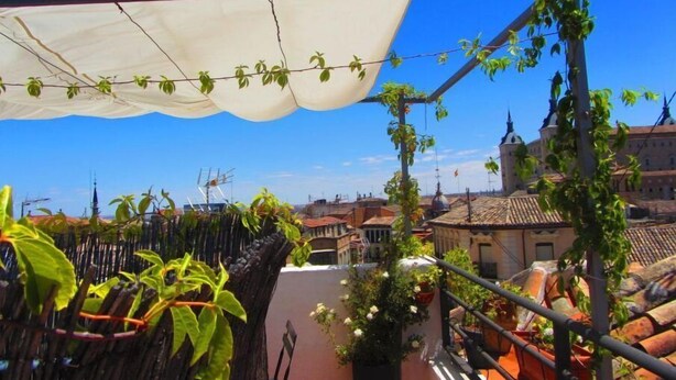 A rooftop terrace with a white canopy, potted plants, and a view of the cityscape.