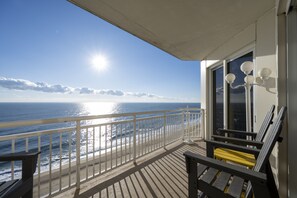 Un balcon avec vue sur l’océan, une balustrade blanche et une chaise jaune.