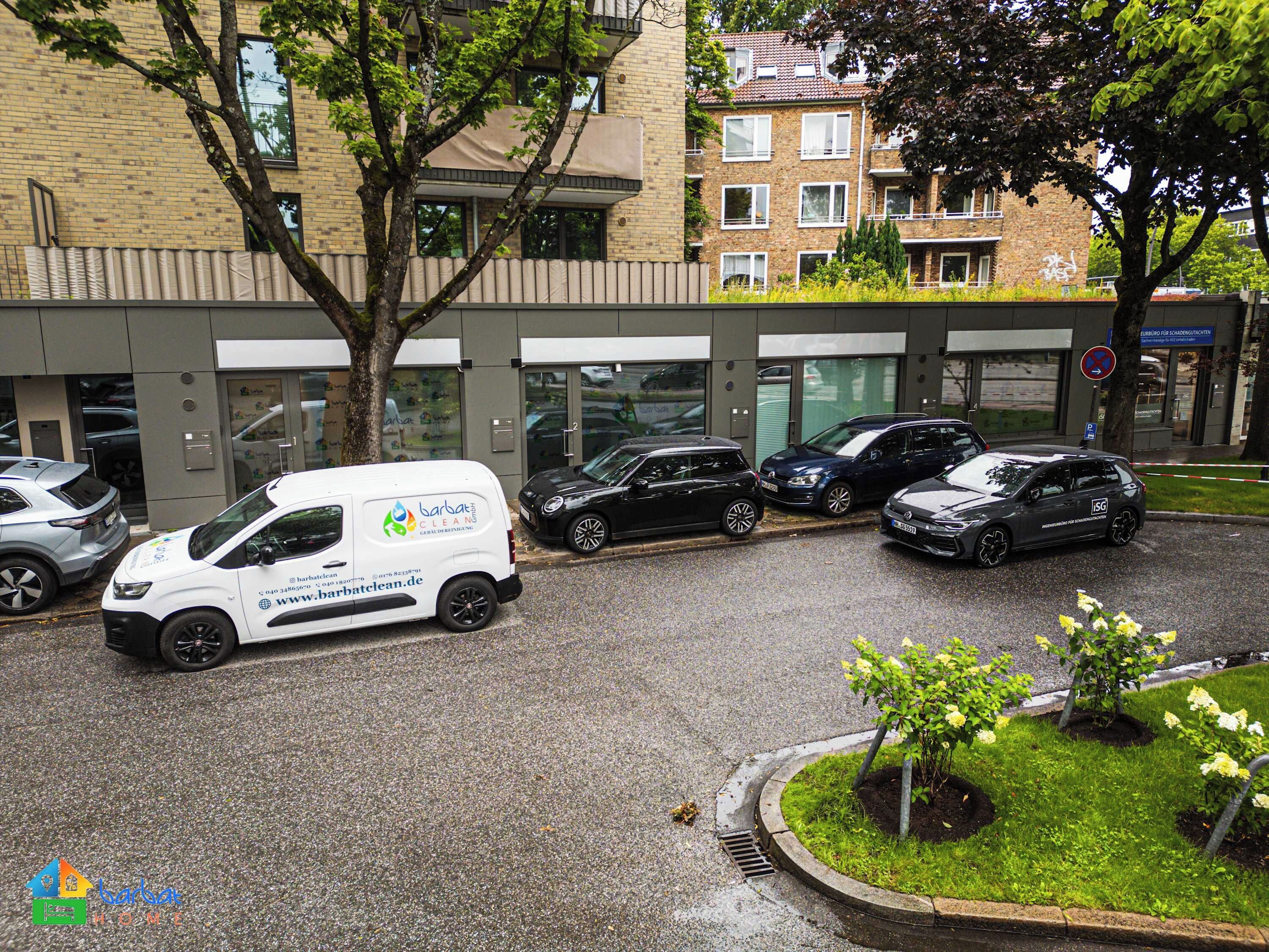 Ein Parkplatz mit einem weißen Lieferwagen, mehreren Autos und einem Gebäude mit vielen Fenstern und einem Schild.