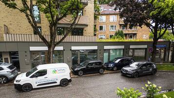 Ein Parkplatz mit einem weißen Lieferwagen, mehreren Autos und einem Gebäude mit vielen Fenstern und einem Schild.