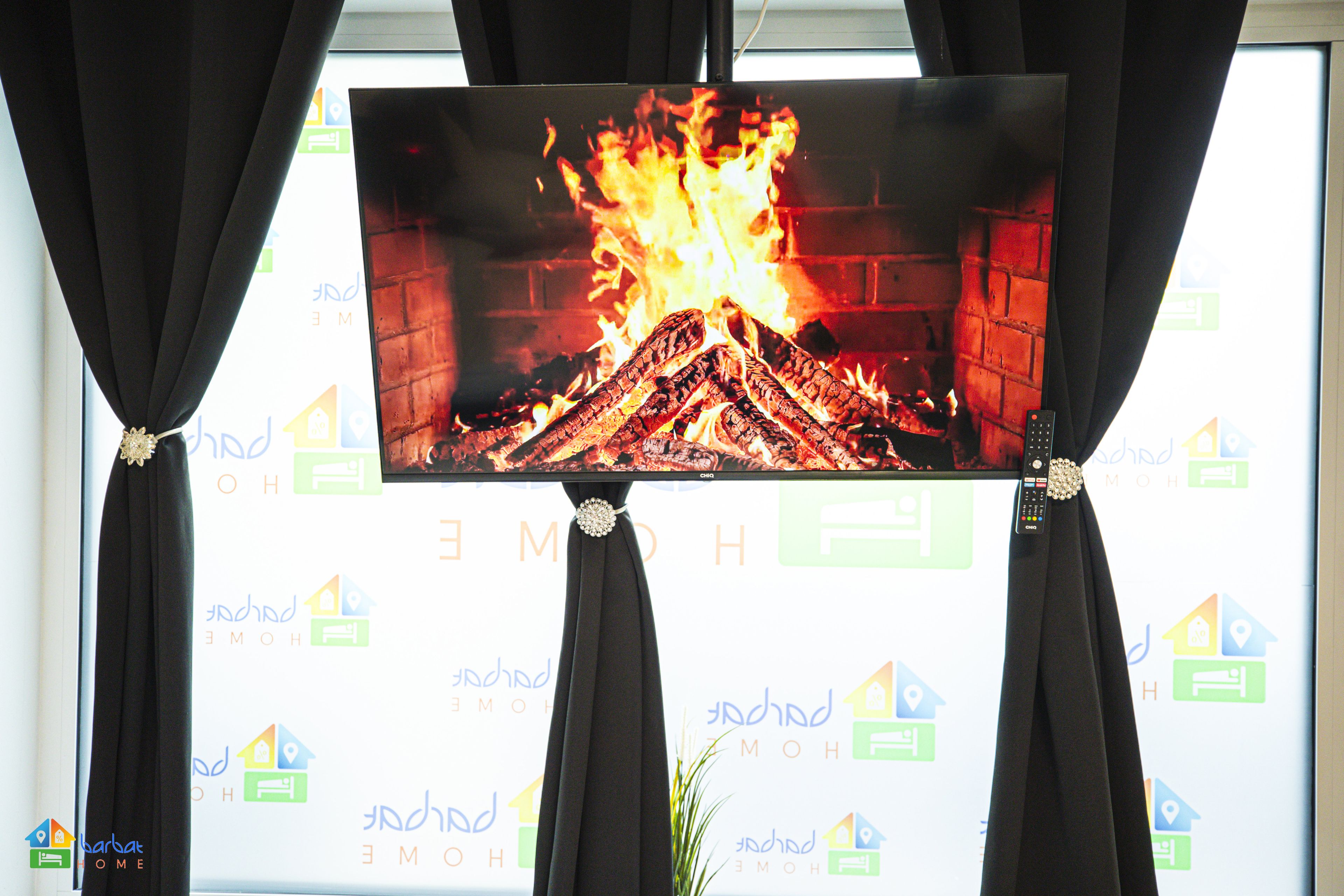 A television displaying a fire scene, mounted on a wall with curtains.