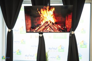 A television displaying a fire scene, mounted on a wall with curtains.