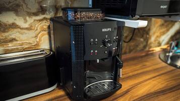 Eine KRUPS Kaffeemaschine steht auf einer Holz Arbeitsplatte, zusammen mit einem Toaster. Im Hintergrund ist eine Wand mit einem marmorähnlichen Muster zu sehen.