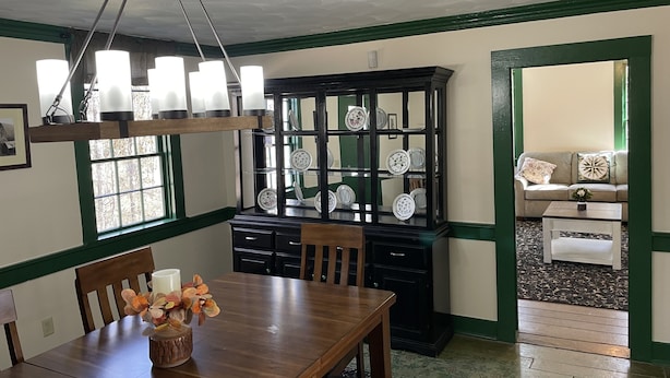 Ein Essbereich mit Holztisch, Stühlen, einer Chandelierleuchtre und einem Schrank mit dekorativen Tellern.