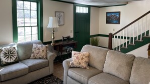 Ein Wohnzimmer mit zwei Sofas, einer Lampe, einer Nähmaschine, einer grünen Tür und einer Treppe.