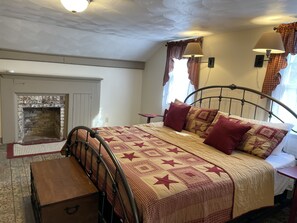 Une chambre à coucher comprenant un lit, une table de chevet, une commode en bois, une cheminée et une fenêtre avec des rideaux.
