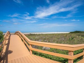 A wooden boardwalk leading to a beach with a clear sky.