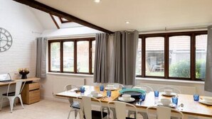 A dining area with a wooden table, white chairs, and a clock on the wall. - Charming Oxford Cottage (Oxfordshire)
