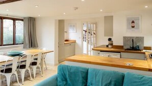 A modern kitchen with a wooden countertop, white cabinets, and a dining area with a table and chairs. - Charming Oxford Cottage (Oxfordshire)