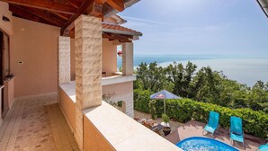 A pool area with a view of the sea, stone pillars, and outdoor furniture. - Stunning home in Veprinac with sauna (Veprinac)