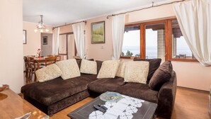 A cozy living room with a brown sofa, a dining area with a table and chairs, and large windows with curtains. - Stunning home in Veprinac with sauna (Veprinac)
