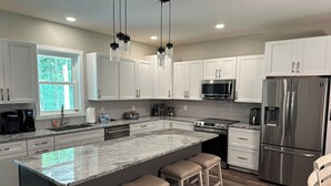 A modern kitchen with white cabinets, a stainless steel refrigerator, a microwave, and a granite island with bar stools. - Hidden Hollow - Your Outdoor destination (Greig)