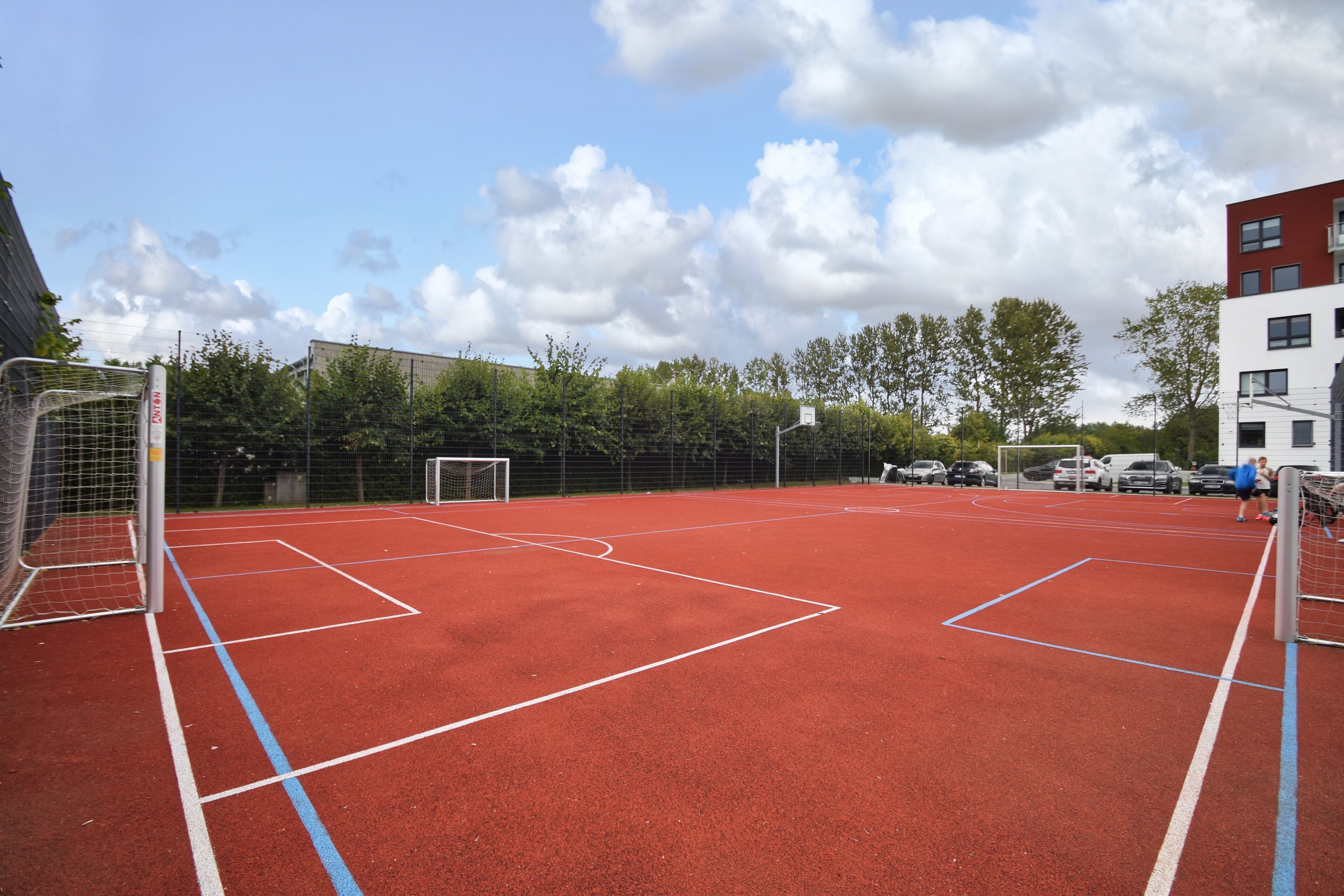 Een buitensportveld met een rode ondergrond, doelen en een net.
