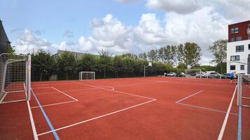 Een buitensportveld met een rode ondergrond, doelen en een net.