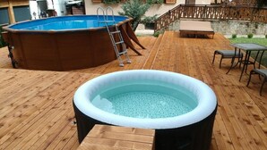 Una terraza exterior de madera con un jacuzzi, un banco de madera y una pequeña mesa.