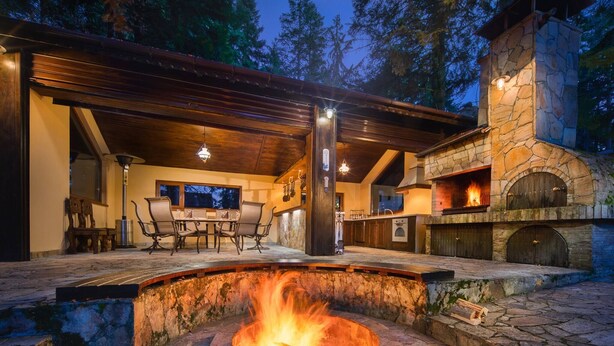 Un patio al aire libre con un pozo de fuego de piedra, un horno de piedra y una zona de estar cubierta.