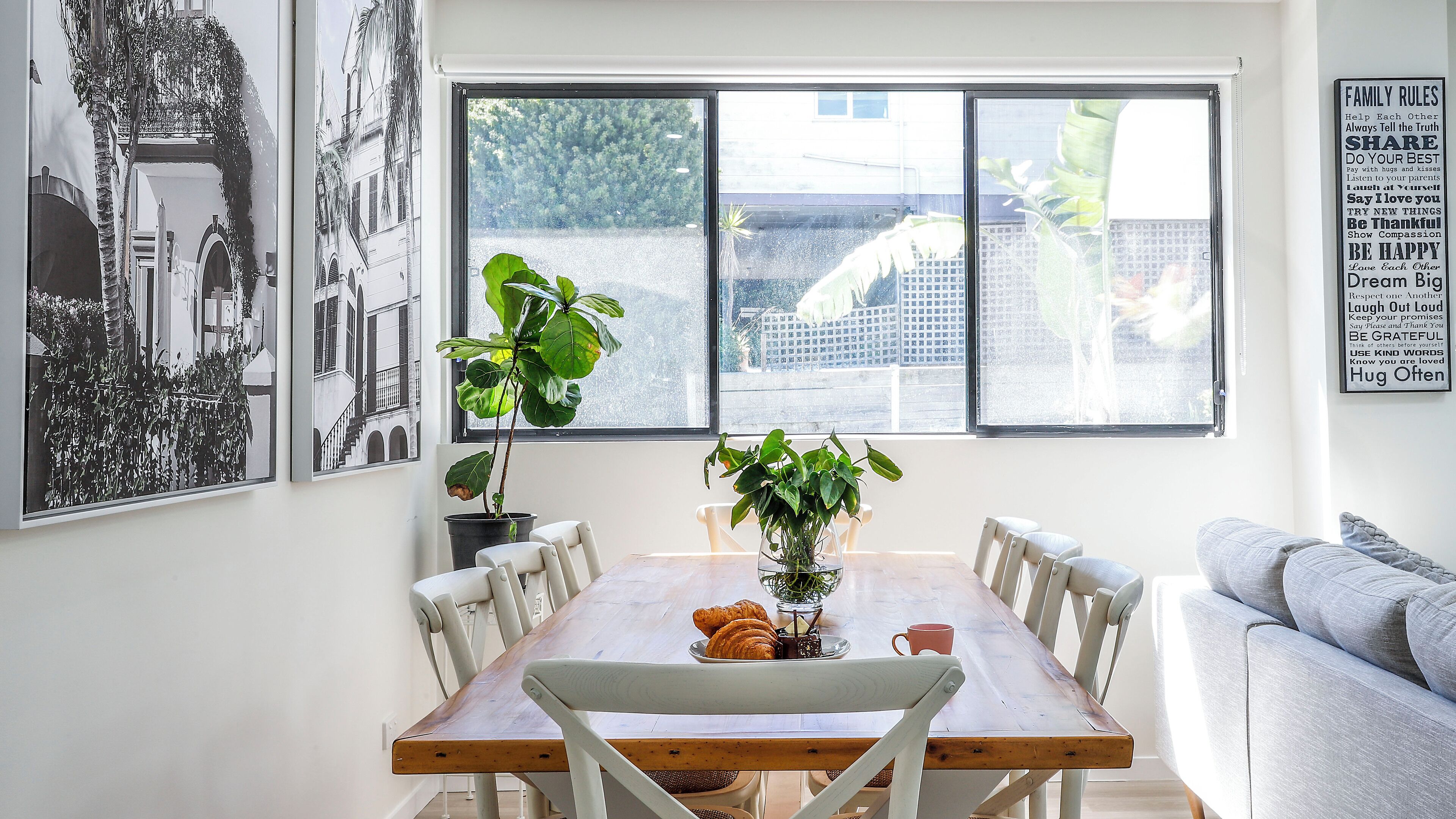 Un coin repas avec une table en bois, des chaises blanches et une plante en pot.