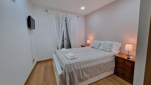 A bedroom with a bed, bedside tables, a TV, and a window with curtains.