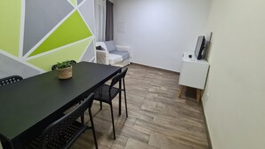 A dining area with a black table and chairs, a small potted plant, and a white sofa in the background.