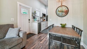 A modern kitchen with white cabinets, a microwave, and a sink. There is a dining table with chairs and a chandelier above it.