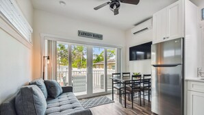 A modern kitchen with a stainless steel refrigerator, a dining area with a table and chairs, and a gray sofa with a remote control on a side table.
