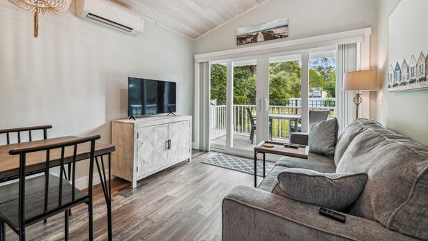 A living room with a sofa, TV, wooden dining table, and a balcony with a view.